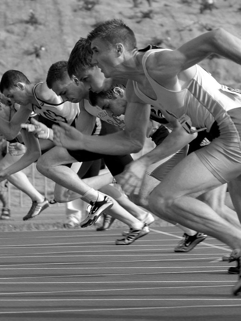 athletes running on track and field oval in grayscale photography